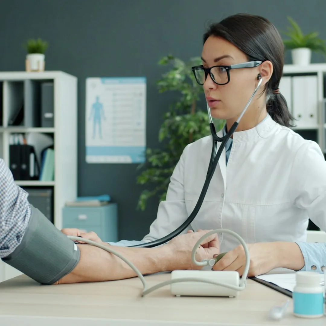 پزشک زن با گوشی پزشکی در حال گرفتن فشار خون یک بیمار مسن در مطب