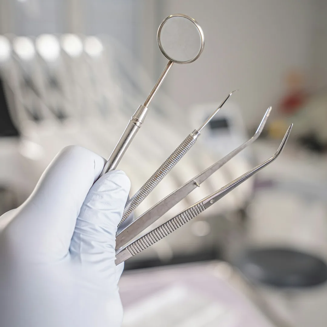 دست دستکش‌پوش دندانپزشک با آینه و ابزار معاینه در مطب