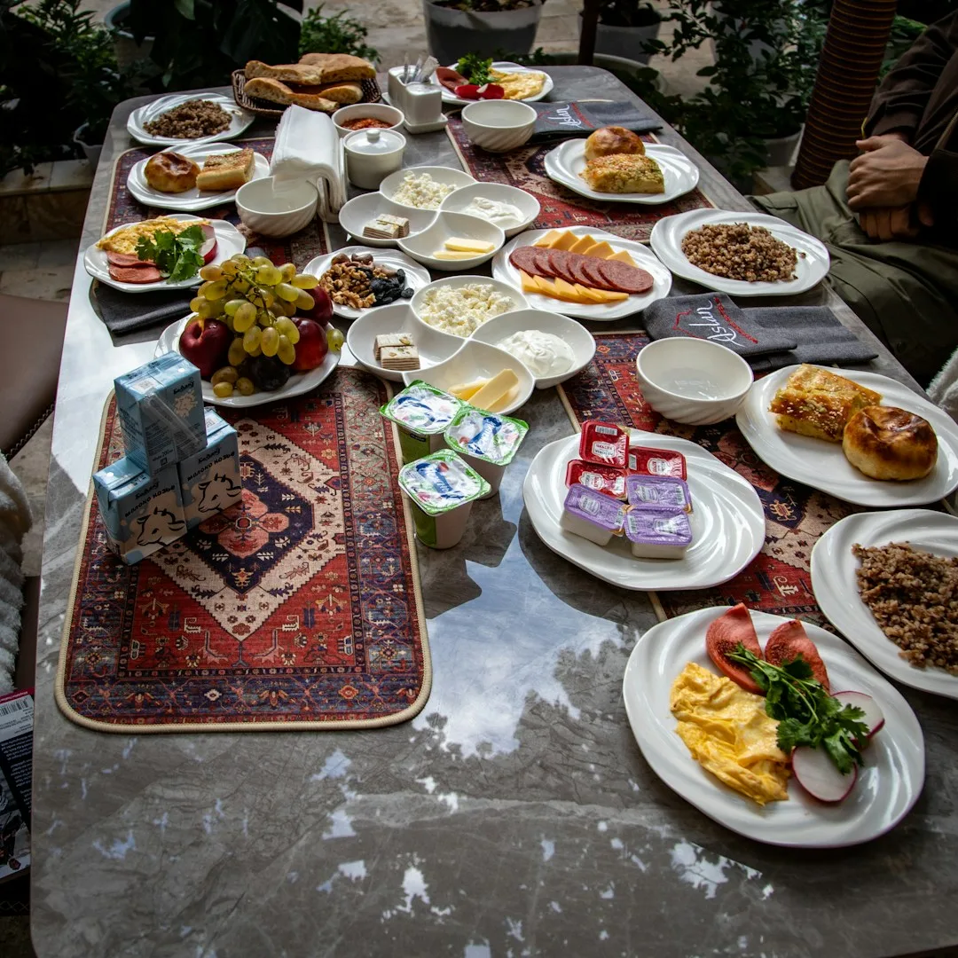 میز بزرگ صبحانه با نان، پنیر، میوه و تخم‌مرغ روی رومیزی ترکمنی